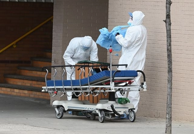 Trabajadores médicos se retiran su traje de protección tras entregar el cadáver de una persona muerta por coronavirus a un camión en Nueva York. Foto Afp