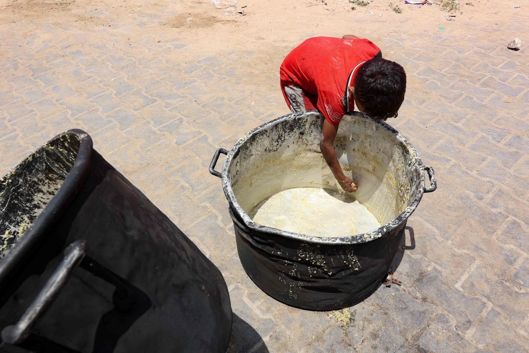 Un niño palestino retira restos de comida de una olla en un punto de distribución de alimentos en un campamento de desplazados, cerca del puerto de Gaza, el 22 de mayo de 2025. Foto  