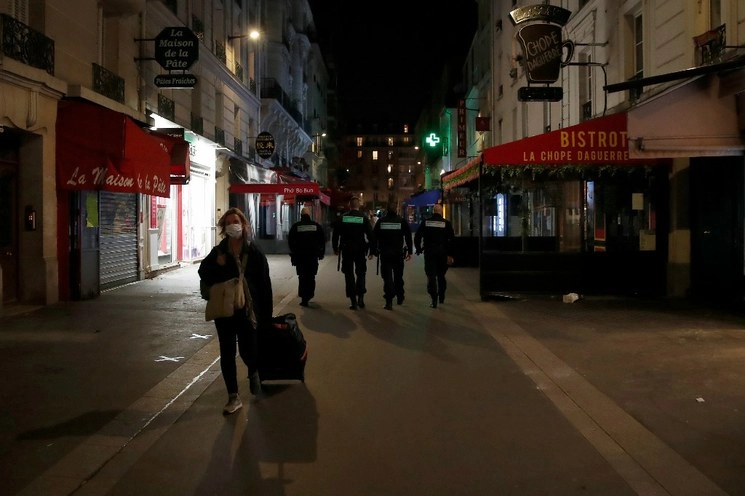 Una mujer con tapaboca camina por las calles den París, dándole la espalda a cuatro policías. Foto Ap