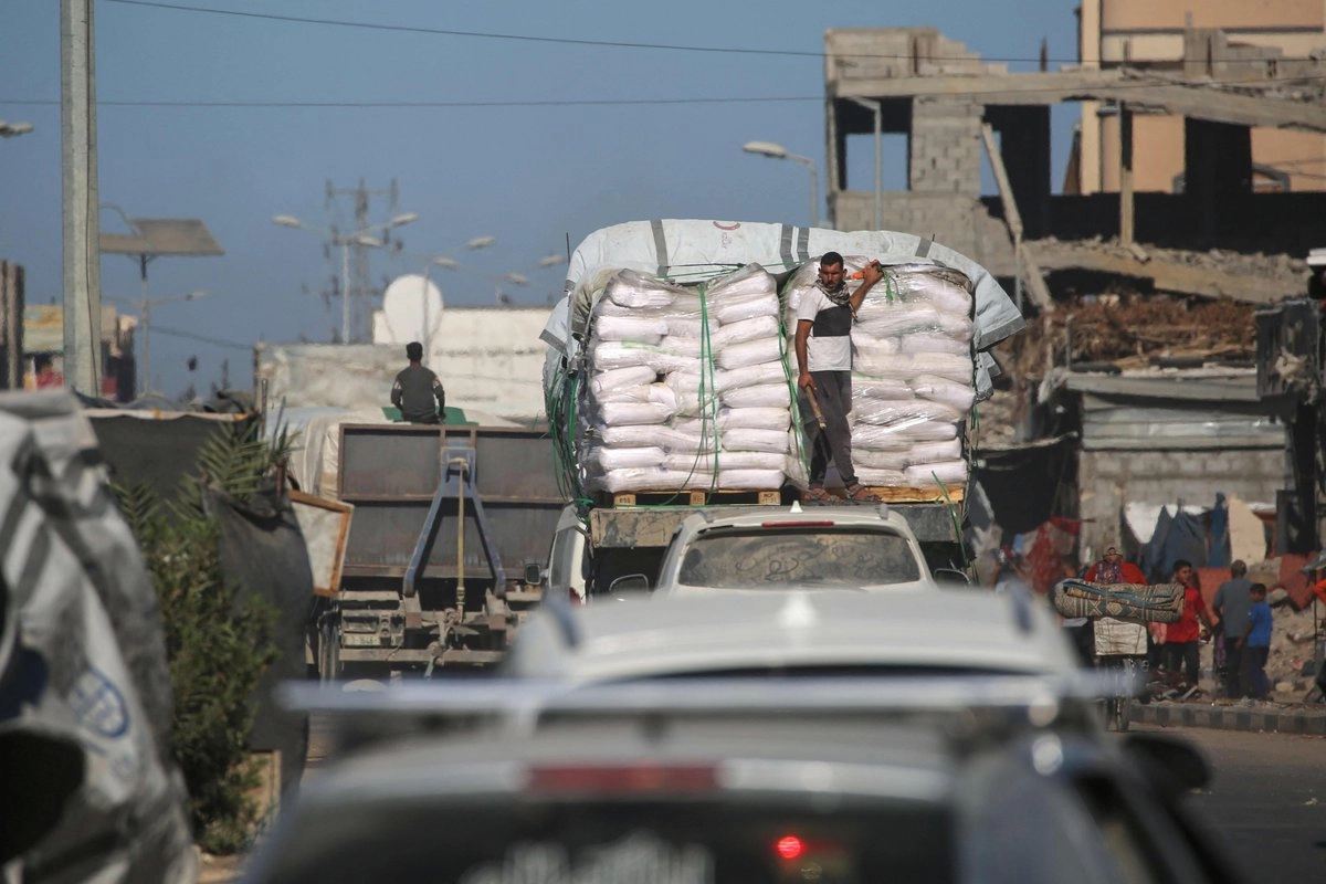camiones con ayuda humanitaria que entraron en Gaza por el cruce de Karm Abu Salem pasan junto a tiendas de campaña para desplazados en el campo de refugiados de Nuseirat, en el centro de la Franja de Gaza, el 14 de octubre de 2025, un día después de la entrada en vigor del alto el fuego entre Israel y las facciones palestinas.