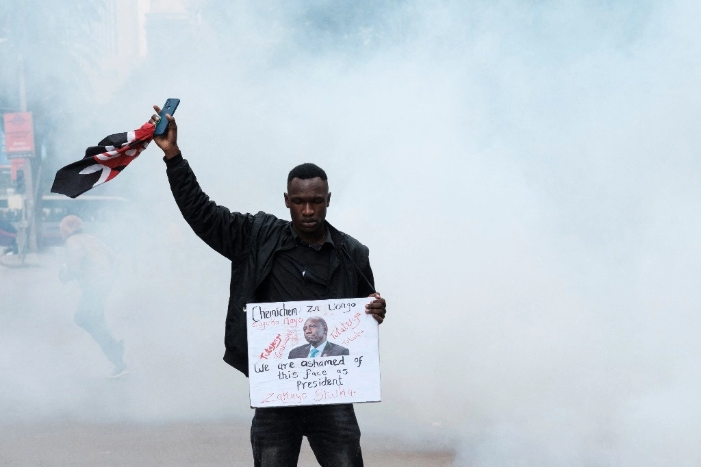 Un manifestante sostiene una pancarta y una bandera de Kenia mientras una nube de gases lacrimógenos lo rodea durante una protesta antigubernamental en Nairobi el 16 de julio de 2024. Foto Afp

