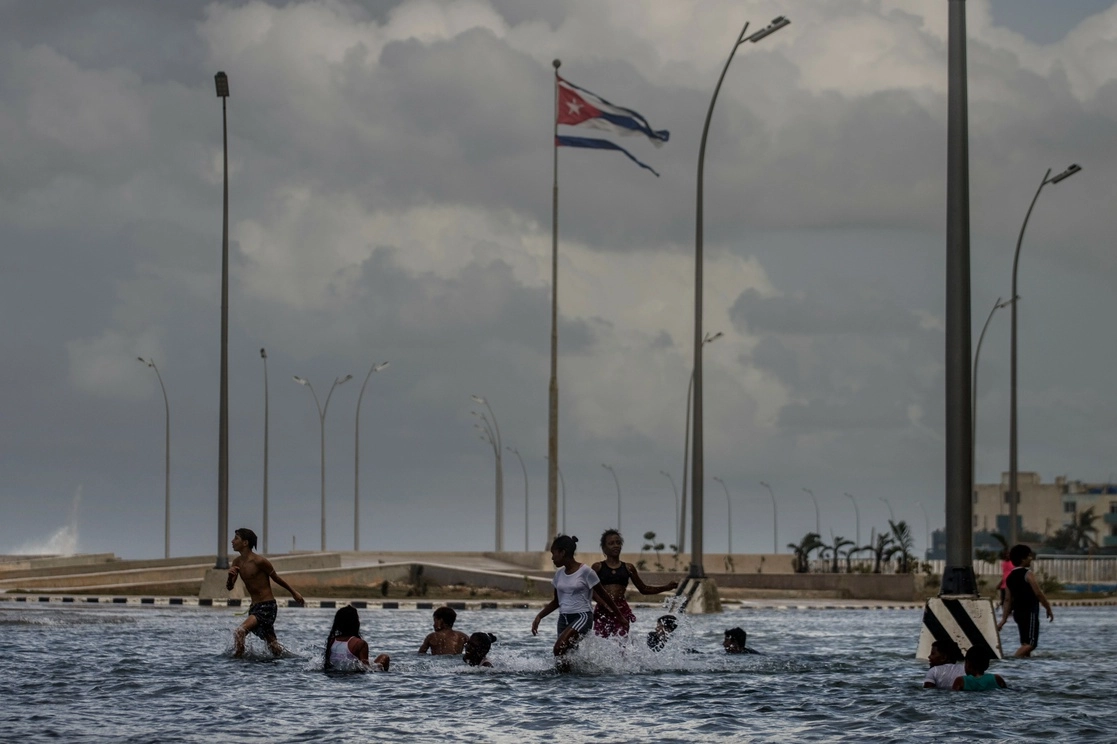 Una bandera cubana, destrozada por los vientos del huracán Ian, ondea en el aire mientras los niños juegan en el agua de mar de las olas rompiendo en el Malecón de La Habana, Cuba, el jueves 29 de septiembre de 2022. Foto Ap