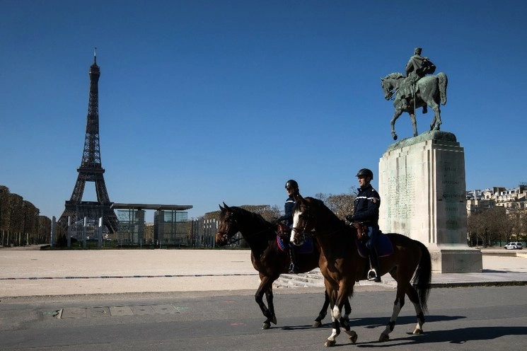Una pareja de policías franceses realizan rondines cerca de la Torre Eiffel, al fondo, en el noveno día de confinamiento en París, cuyo objetivo es frenar la propagación del Covid-19. Foto Afp