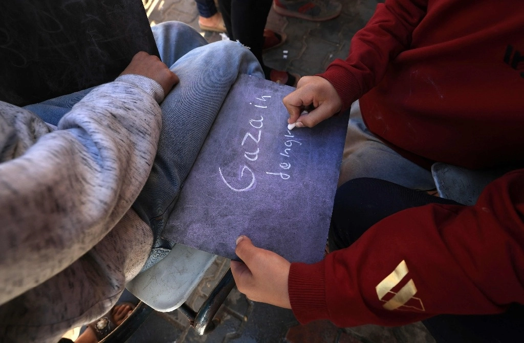 Un niño palestino desplazado escribe en el pizarrón durante una clase de inglés en un albergue temporal en Rafah, en la franja de Gaza, el 29 de noviembre de 2023. Foto Afp