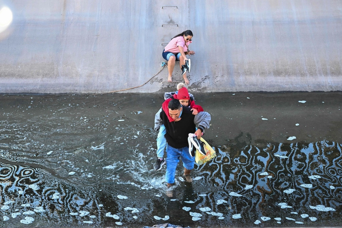 Una familia de migrantes se abre paso en un canal de agua en El Paso, Texas, después de cruzar por debajo de un agujero en el muro fronterizo entre México y EU. Foto Afp



