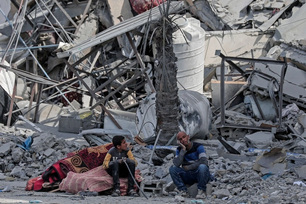 Palestinos desplazados esperan con sus pertenencias entre los escombros de sus casas destruidas por un bombardeo israelí, en el área de Hamad, al oeste de Jan Yunis, al sur de Gaza, este jueves. Foto Afp 