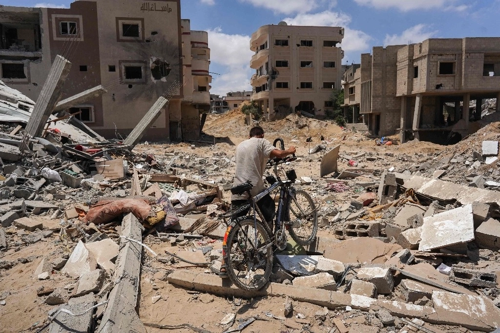 Un hombre empuja su bicicleta sobre los escombros mientras los palestinos desplazados regresan a Bani Suhayla y a las ciudades vecinas al este de Khan Yunis tras los informes de que las fuerzas israelíes se retiraban de la zona en el sur de la Franja de Gaza el 30 de julio de 2024. Foto Afp