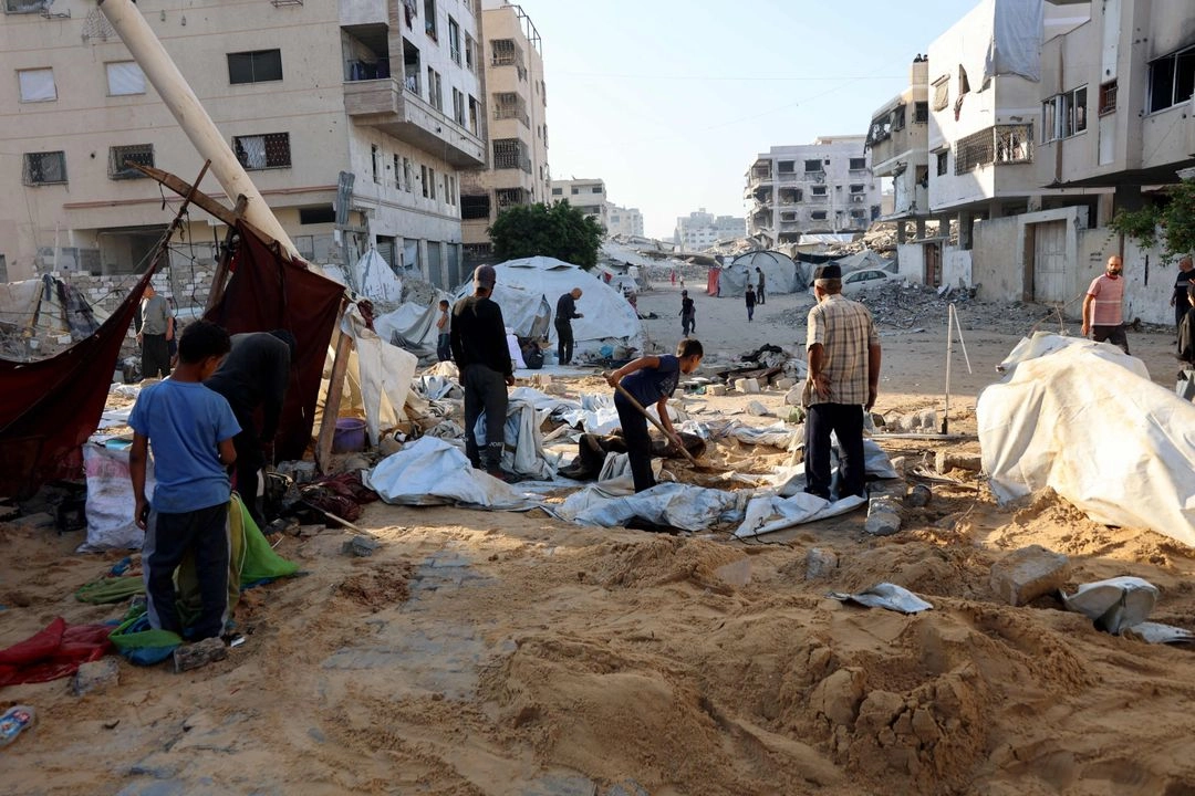 Palestinos retiran la arena que cubre las tiendas de campaña después de que el ejército israelí atacara personas desplazadas en el barrio norteño de Al-Rimal, en la ciudad de Gaza, el 28 de junio de 2025.