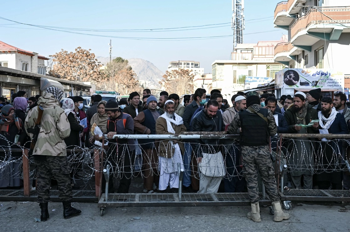 Un combatiente talibán inspecciona los documentos de las personas que hacen fila para ingresar a la oficina de pasaportes en Kabul el 18 de diciembre de 2021. Foto Afp