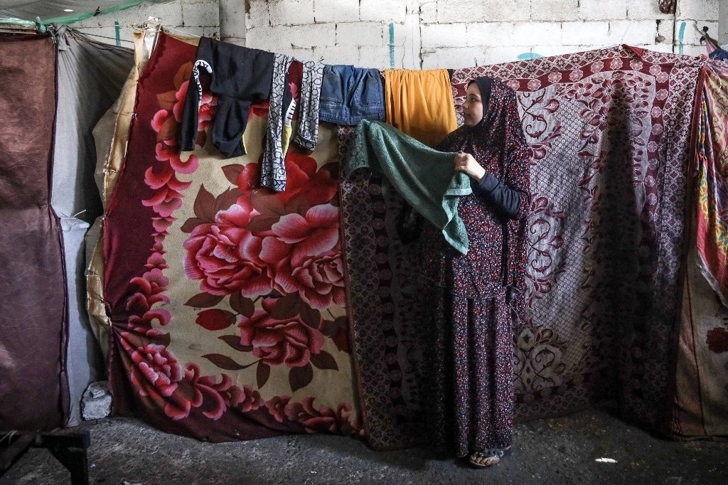 Una mujer palestina embarazada desplazada del norte de Gaza cuelga ropa en un almacén donde se refugia en Rafá, en el sur de la Franja de Gaza, el 29 de febrero de 2024, en medio de las batallas en curso entre Israel y el movimiento palestino Hamas. Foto Afp