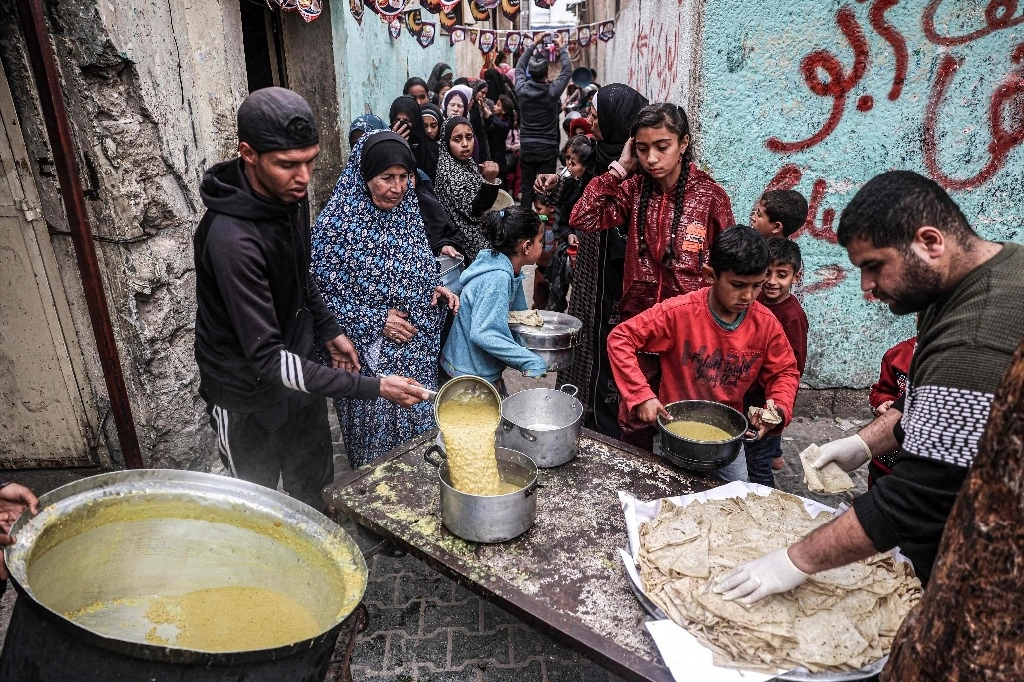 Miles de palestinos desplazados reciben alimentos donados antes de la comida iftar para romper el ayuno durante el mes sagrado musulmán del Ramadán, en Rafah, Gaza. Foto Afp
