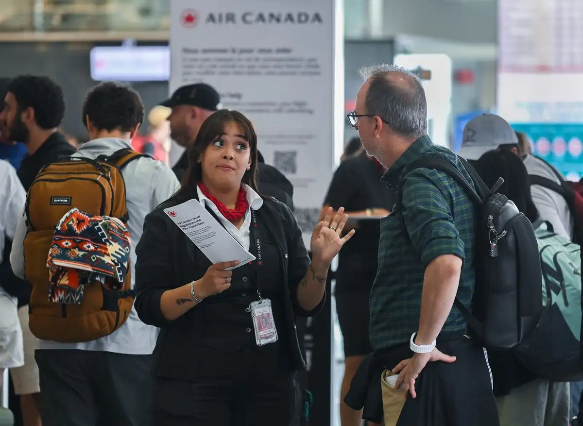 Un agente de Air Canada, a la izquierda, conversa con un hombre durante la huelga de auxiliares de vuelo de Air Canada en el Aeropuerto Internacional Pierre Elliott Trudeau de Montreal, el sábado 16 de agosto de 2025. Foto