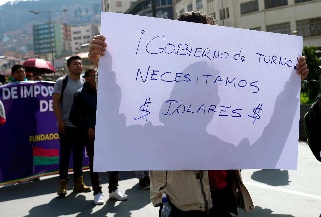 Un comerciante sostiene un cartel con un mensaje que dice en español: "Gobierno actual, necesitamos dólares¡" durante una protesta en La Paz, Bolivia, el viernes 17 de mayo de 2024. Foto Afp