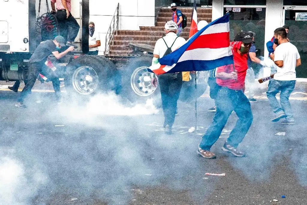 Manifestantes tratan de alejarse de gases lacrimógenos lanzados por la policía, en San José, Costa Rica, el 12 de octubre de 2020, durante protestas contra el intento del gobierno de aumentar impuestos para alcanzar un crédito del FMI. Foto Afp