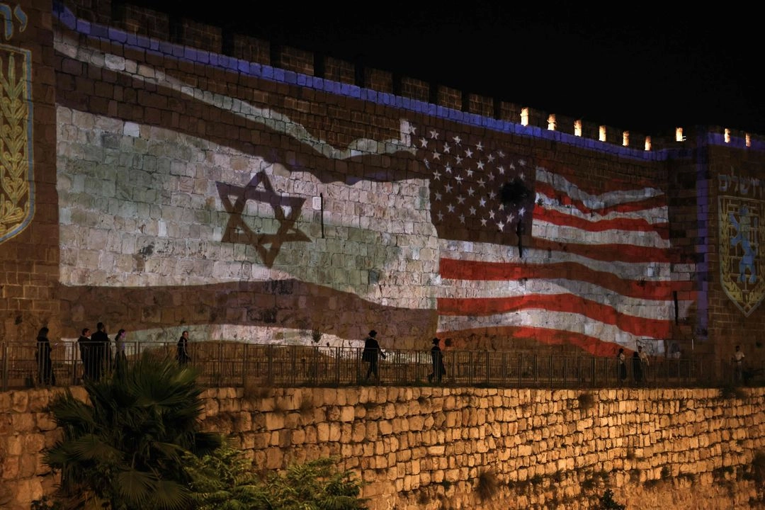 La gente pasa junto a una proyección que representa las banderas israelí y estadunidense en los muros de la Ciudad Vieja de Jerusalén, el 22 de junio de 2025. 