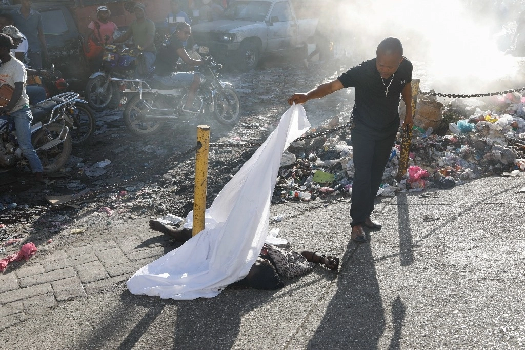 Una persona levanta una sábana para identificar a un cuerpo que yace sobre el asfalto, tras el tiroteo nocturno en el vecindario de Petion Ville, en Puerto Príncipe, Haití. Foto Ap 