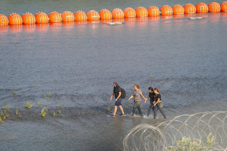 Migrantes caminan cerca del muro de boyas colocado a lo largo de la frontera de Río Grande con México, el 16 de julio de 2023. Foto Afp
