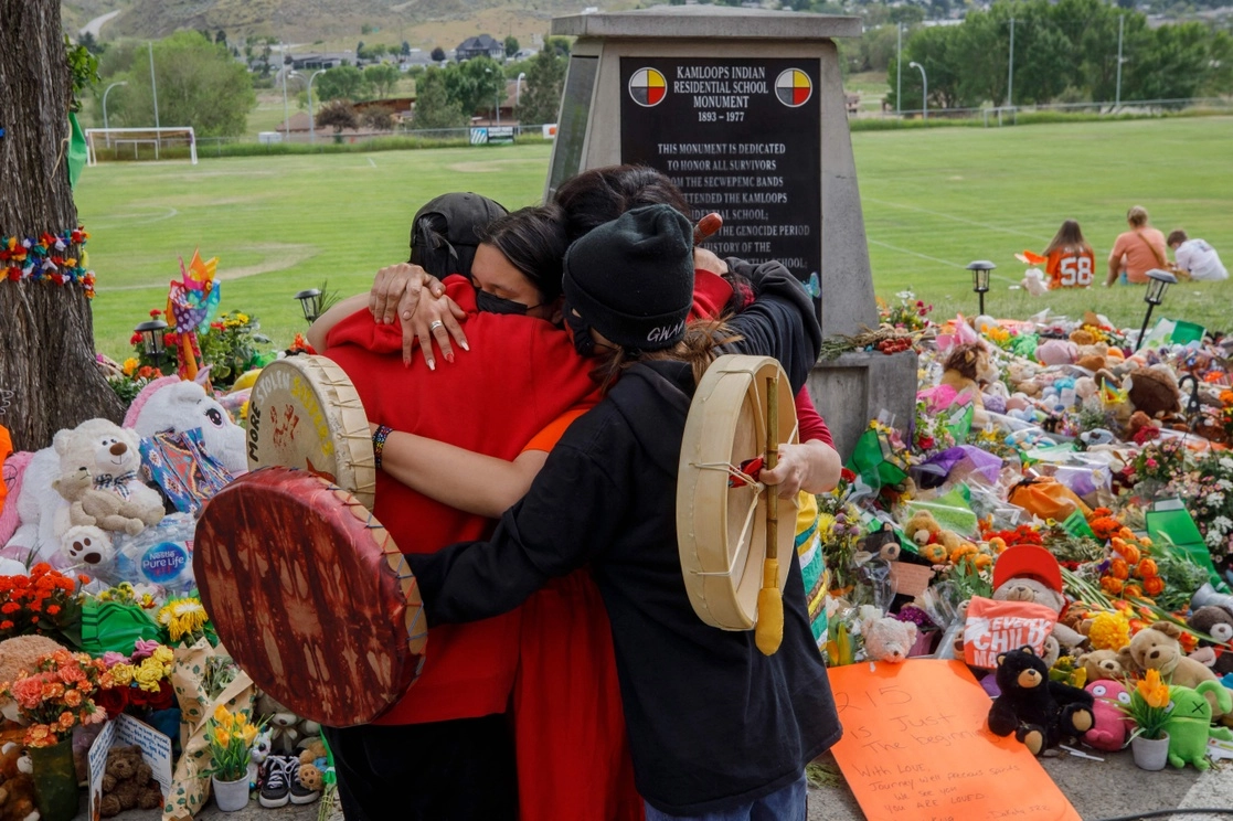 Indígenas de la nación de los Mosakahiken se abrazan frente a un memorial para honrar a los 215 niños, cuyos restos fueron hallados en Canadá cerca de un internado, el pasado 4 de junio. Foto Afp 
