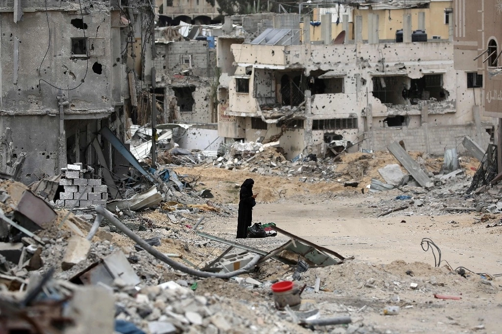 Una mujer palestina revisa su teléfono celular, en medio de un vecindario devastado por un bombardeo israelí en Jan Yunis, al sur de la franja de Gaza. Foto Afp