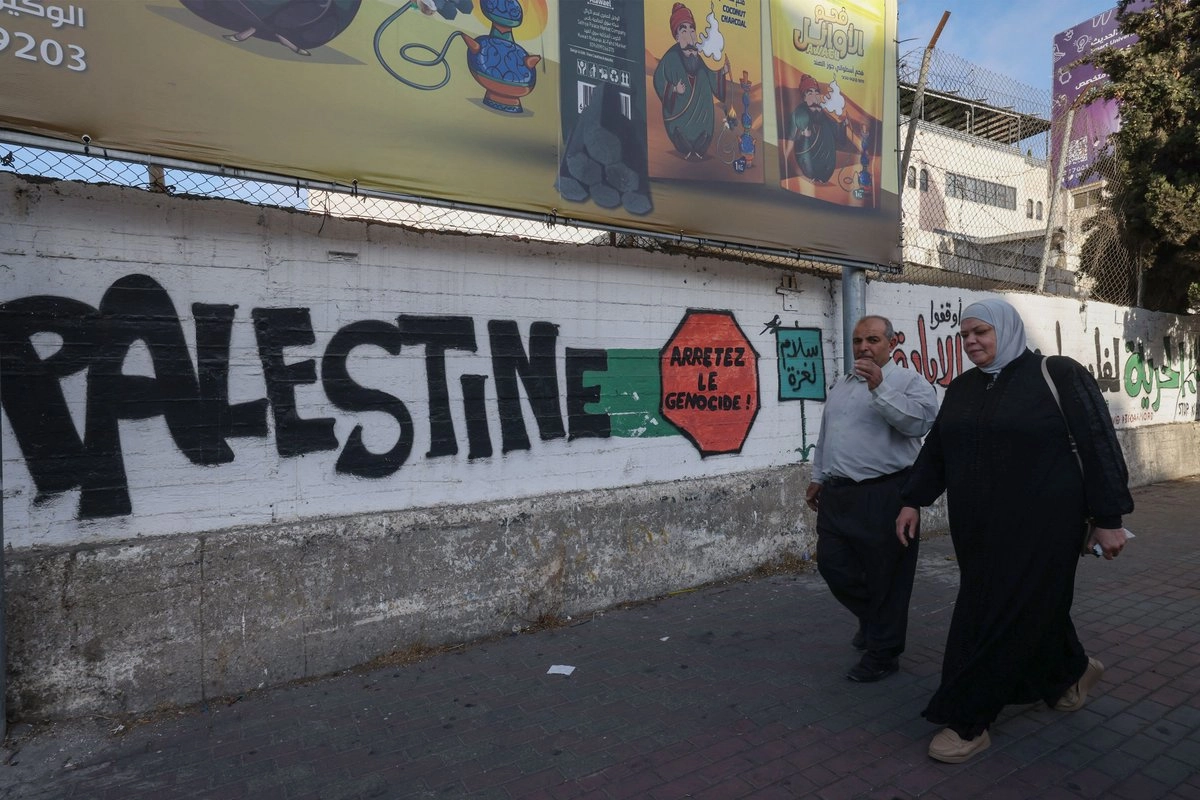 Palestinos caminan junto a un grafiti que pide la paz en Gaza y el fin del genocidio en un muro de Hebrón, en Cisjordania ocupada, el 6 de octubre de 2025. Foto 