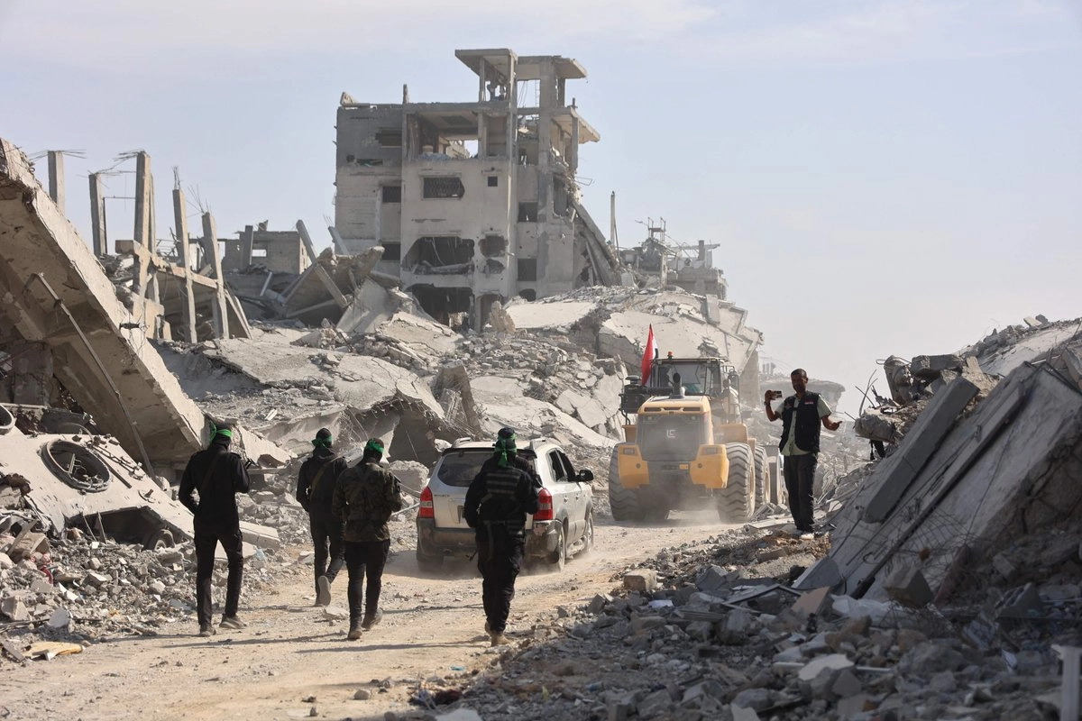 Militantes palestinos armados de Hamas, junto con miembros de la Cruz Roja Internacional (CICR), siguen a una excavadora suministrada por Egipto durante la búsqueda de los cuerpos de los rehenes israelíes asesinados en la ciudad de Gaza, el 2 de noviembre de 2025.