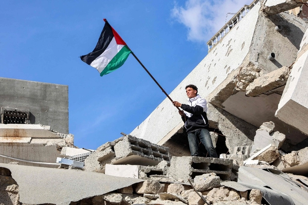 Un joven ondea una bandera palestina sobre los escombros de un edificio devastado por los bombardeos israelíes en Jabaliya. Foto Afp