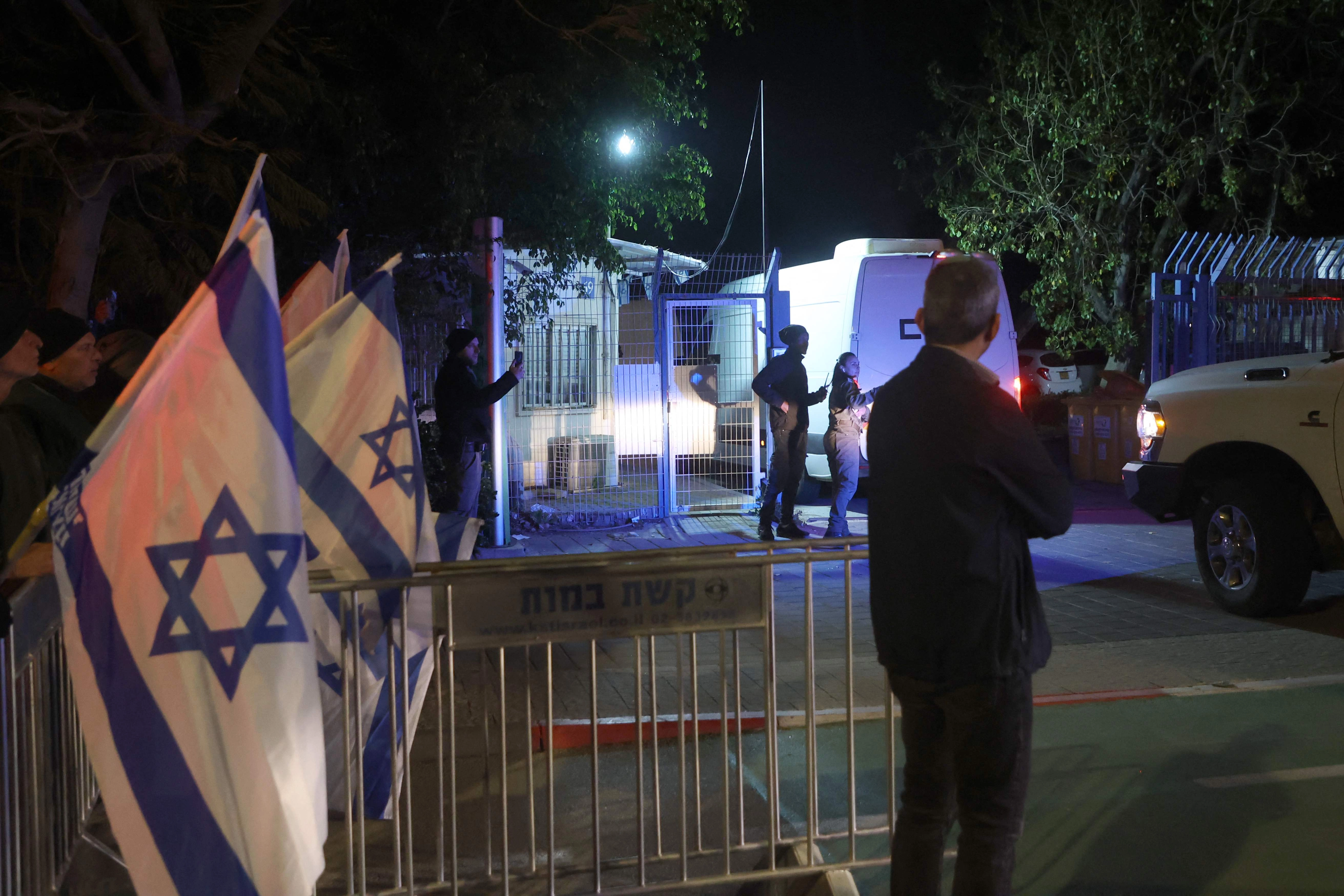 Israelíes ondean la bandera nacional mientras observan el convoy de vehículos que transportan los cuerpos de los cuatro rehenes israelíes entregados por Hamas, ingresar al Centro Nacional de Medicina Forense en Tel Aviv el 27 de febrero de 2025. Foto 