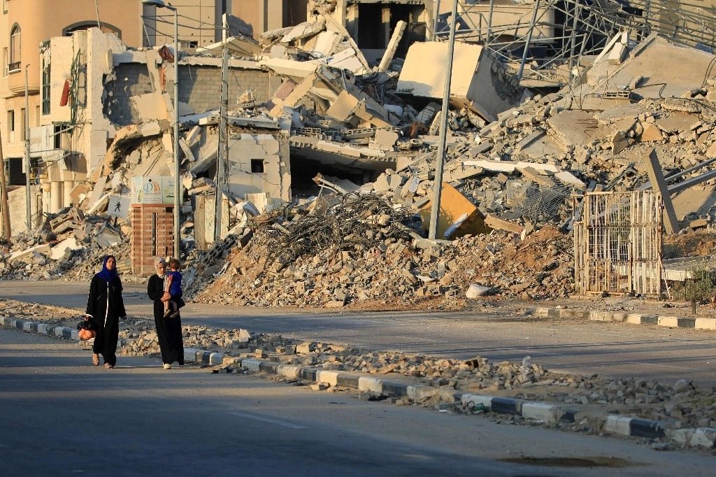 Palestinos desplazados caminan junto a edificios destruidos en el campo de refugiados de Al-bureij, en el centro de la franja de Gaza. Foto Afp