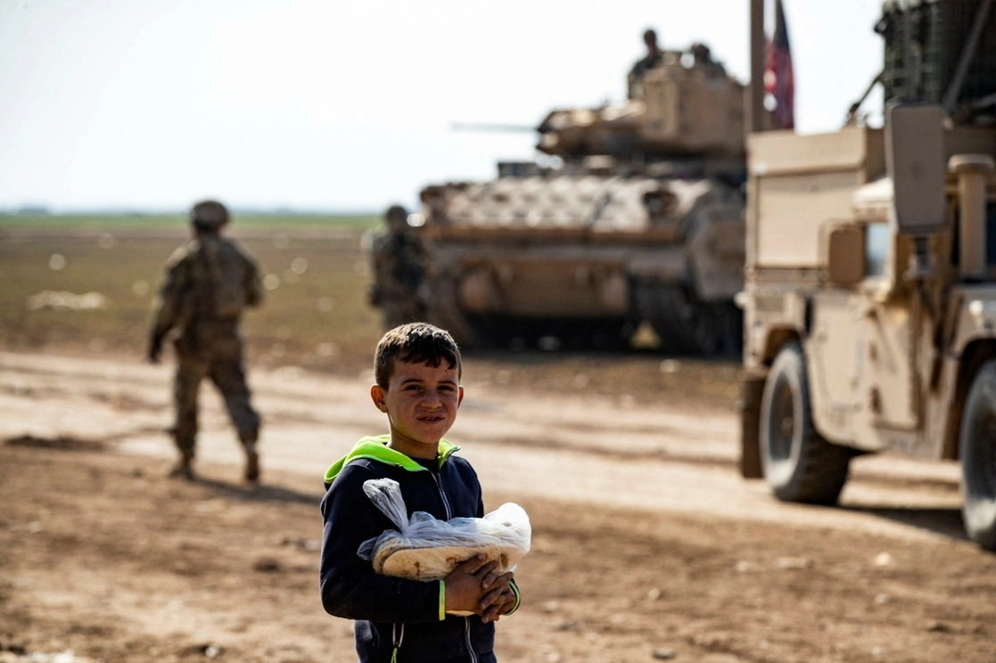 Un niño sirio sostiene una barra de pan al paso de un convoy de militares estadunidenses en las cercanías de la ciudad de Qameshli. Foto Afp.