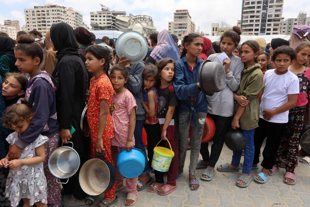 Niñas y niños palestinos hacen fila frente a un camión de reparto de comida caliente en un campamento de desplazados cerca del puerto de Gaza, el 22 de mayo de 2025. Foto 