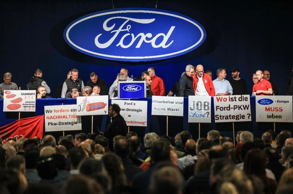 Empleados del gigante automovilístico estadounidense Ford posan con sus carteles en el escenario antes de una reunión de trabajo el 27 de noviembre de 2024 en la planta de la compañía en Colonia, en el oeste de Alemania. Foto Afp