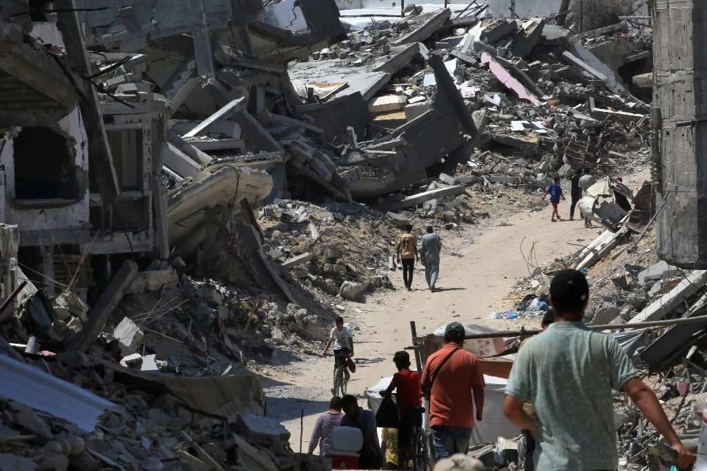 La gente camina por una carretera entre los escombros de los edificios destruidos durante el bombardeo israelí en Khan Yunis, en el sur de la Franja de Gaza, el 23 de junio de 2024, en medio del conflicto en curso entre Israel y el grupo militante palestino Hamas. Foto Afp