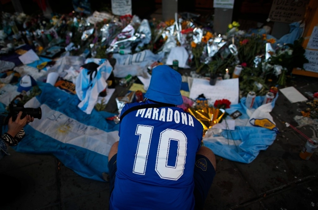 Un fanático llora frente a las flores y carteles en homenaje a Diego Maradona colocados en la entrada del estadio de Boca Juniors. Foto Ap