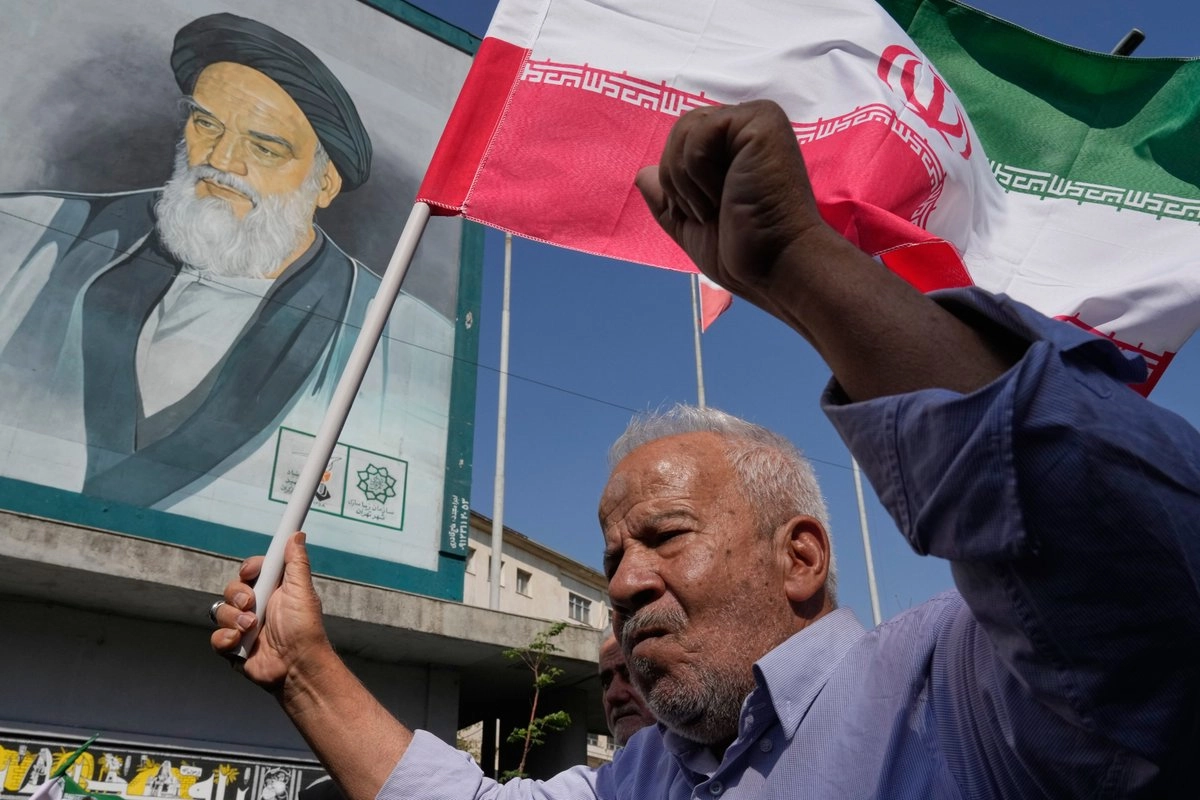 Un fiel iraní sostiene la bandera de su país frente a un retrato del difunto fundador revolucionario, el ayatolá Jomeini. 
