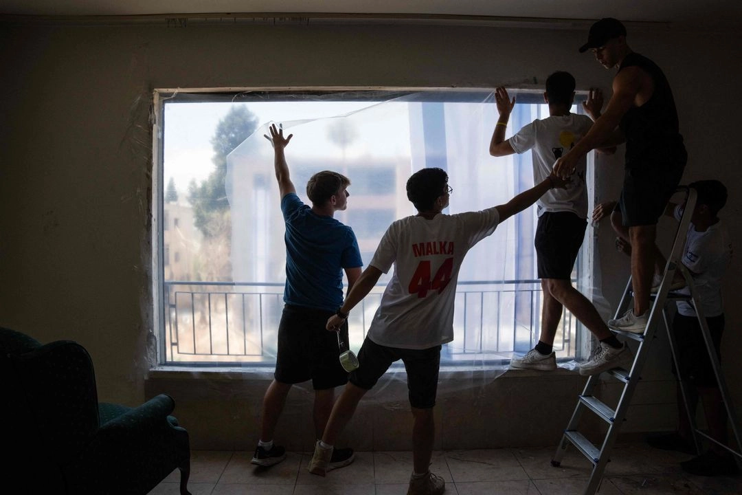 Voluntarios ayudan a cubrir ventanas con plástico luego de que fueran bombardeadas en un ataque con misiles iraníes en Haifa, el 17 de junio de 2025.