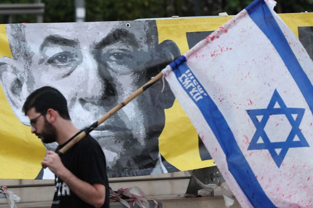 Un manifestante con la bandera israelí pasa junto a un retrato del primer ministro Benjamin Netanyahu durante una protesta antigubernamental que exige la liberación de los rehenes israelíes cautivos desde los ataques del 7 de octubre de 2023 perpetrados por militantes palestinos. Foto