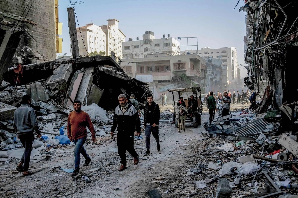 Palestinos caminan entre los escombros de los edificios destruidos en la ciudad de Gaza, en el norte de la franja de Gaza, tras el acuerdo de tregua por cuatro días. Foto Afp