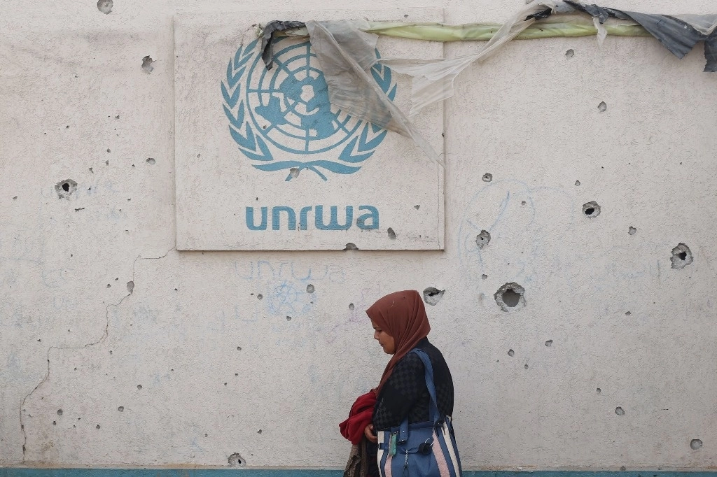 	
Una mujer palestina pasa junto a un muro dañado que lleva el logotipo de la UNRWA en un campamento para desplazados internos en Rafah, en el sur de la Franja de Gaza, el 28 de mayo de 2024, en medio del conflicto en curso entre Israel y el grupo militante palestino Hamas. Foto Afp