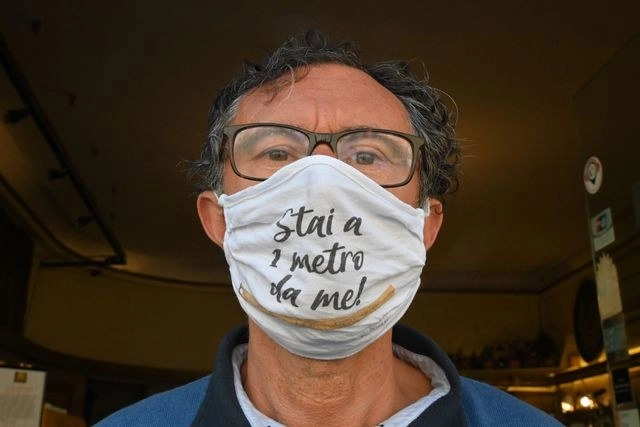El dueño de una cafetería italiana posa con un cubrebocas en el que se lee “Manténte a un metro de mí”, en Roma. Foto Afp