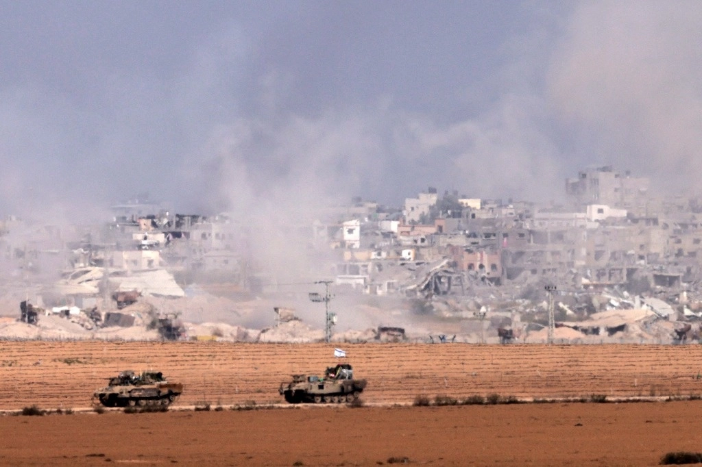 En imagen captada ayer desde el sur de Israel, cerca de la frontera con la franja de Gaza, se observan vehículos blindados israelíes a lo largo de la valla fronteriza, mientras el humo se eleva sobre el enclave palestino en medio de batallas en curso con el grupo yihadista Hamas. Foto Afp 
