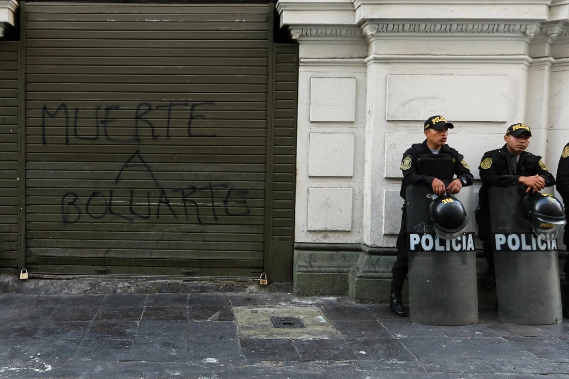 Policías antidisturbios de Perú montan guardia junto a un grafiti contra la Presidenta. Foto Afp