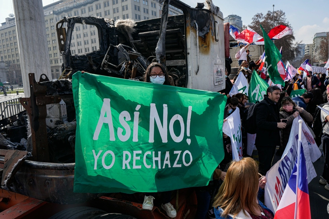 Junto a un camión supuestamente incendiado por indígenas mapuche que exigían la devolución de sus tierras, manifestantes rechazaron el proyecto de Constitución frente al palacio presidencial de La Moneda, en Santiago, hace unos días. Foto Ap
