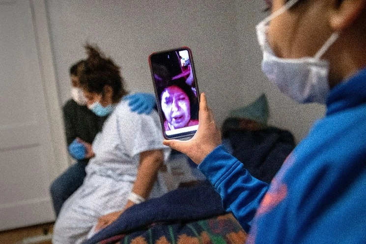 Junior, de 7 años, le permite a su abuela mirar en una video llamada, mientras su madre Zully, quien padece Covid-19, y su padre Marvin se abrazan después de que Zully regreso a casa del hospital. Foto AFP
