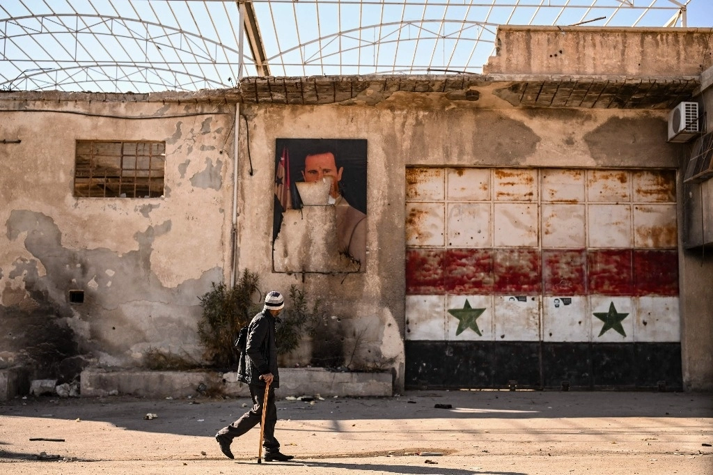 Un hombre pasa junto a un retrato profanado del derrocado presidente Bashar al-Assad en la ciudad de Adra, en las afueras del noreste de Damasco, el 16 de diciembre de 2024. Foto Afp
