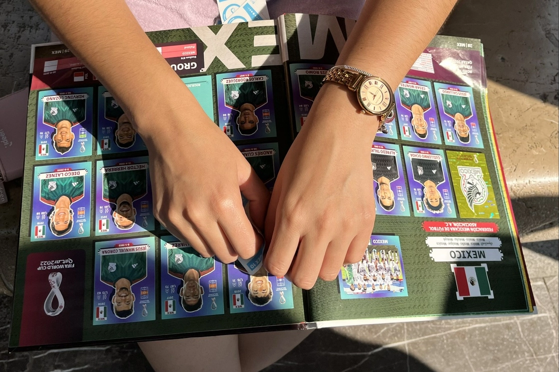 Un coleccionista del álbum Panini del Mundial de Qatar pega las estampas de los jugadores de la selección mexicana a las afueras del Palacio de Bellas Artes, sitio donde se da el intercambio y venta de sobres y estampas sueltas para llenar el álbum. Foto Luis Castillo.