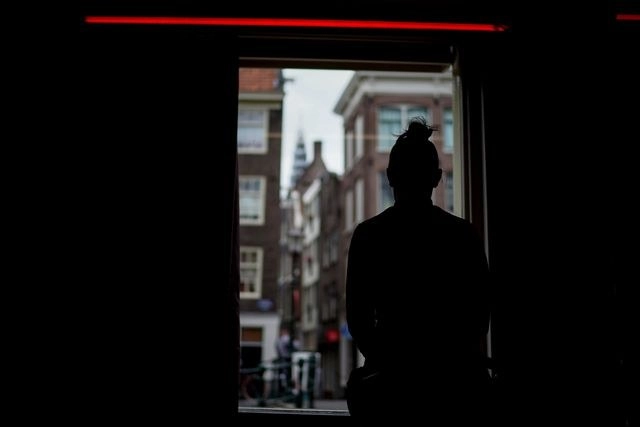 Una prostituta espera clientes detrás de una ventana del distrito rojo de Ámsterdam. Foto Afp 