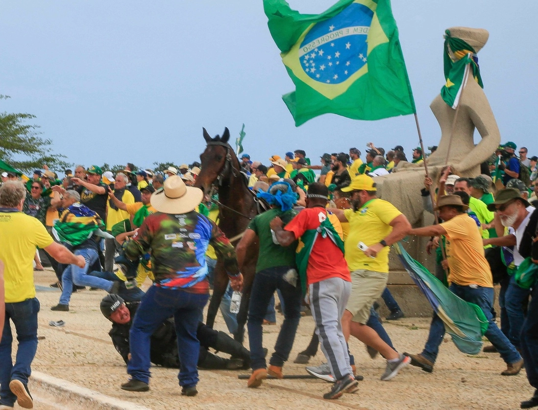 Partidarios de Jair Bolsonaro patean a un policía que cayó de su caballo, durante la invasión al Palacio Presidencial, en Brasilia. Foto Afp