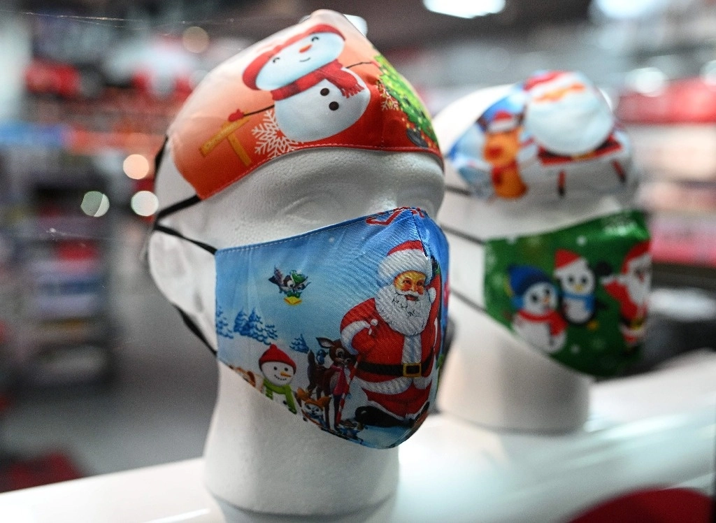Cubrebocas con motivos navideños se exhiben para la venta en el escaparate de una tienda en Manchester, Inglaterra. Foto Afp
