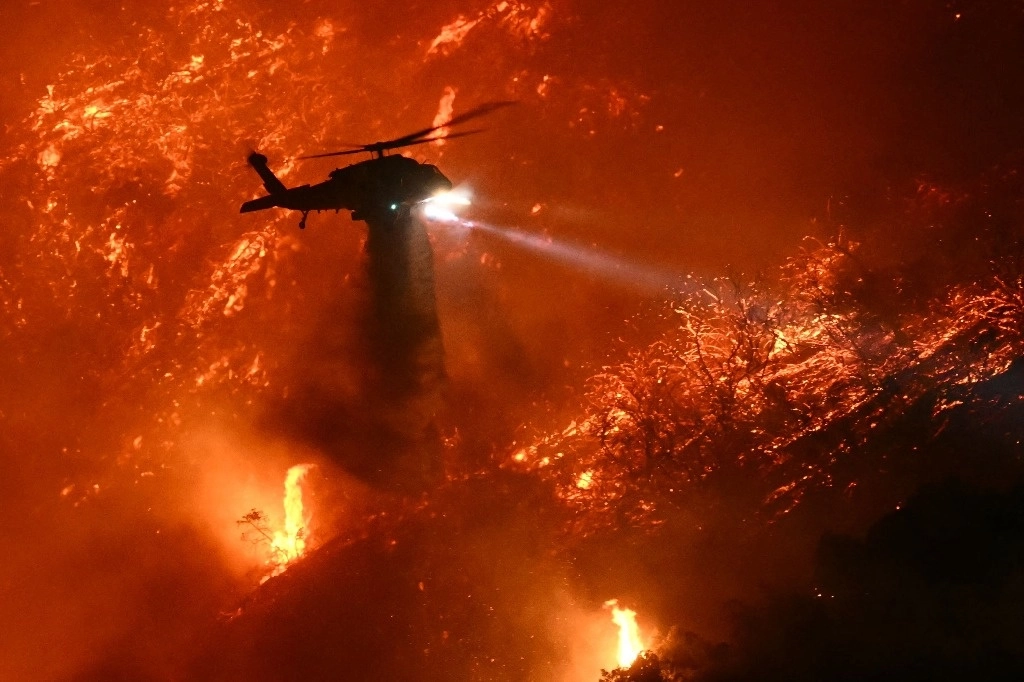 Un helicóptero arroja agua en la zona de Palisades mientras las llamas se acercan a los barrios de Mandeville Canyon y Encino, en California. Foto Afp 