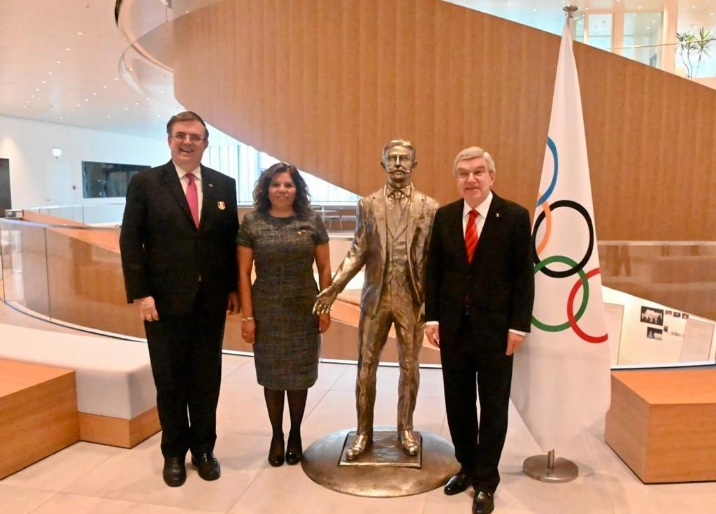 El canciller Marcelo Ebrard, María José Alcalá, titular del COM, y Thomas Bach, presidente del COI, flanquean una estatua del barón Pierre de Coubertin, creador del movimiento olímpico. Foto tomada de Twitter @m_ebrard